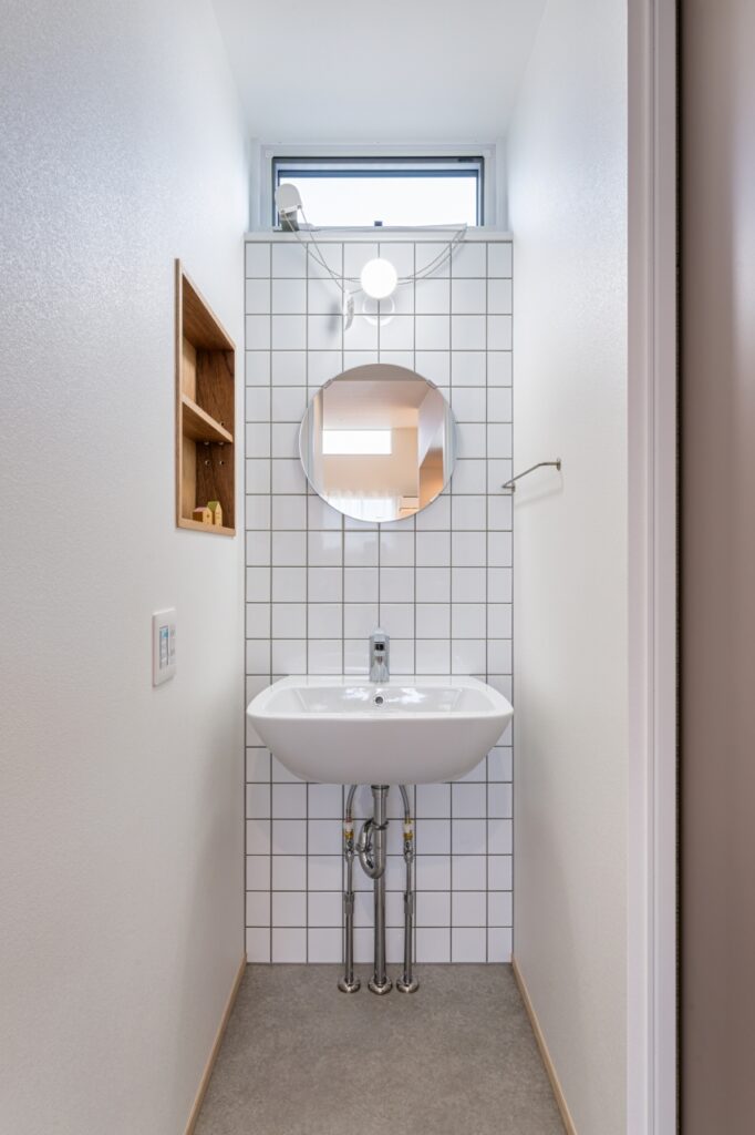 洗面器やタイルを白で統一した洗面室。丸形の鏡が柔らかさを生み出す